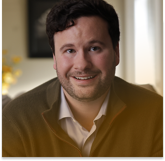 Man in a white button-down and brown sweater smiling