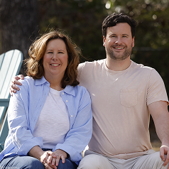Woman in blue button-down and man in a beige shirt with his arm around her sitting together