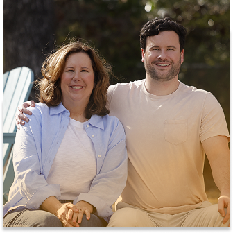 Woman in blue button-down and man in a beige shirt with his arm around her sitting together